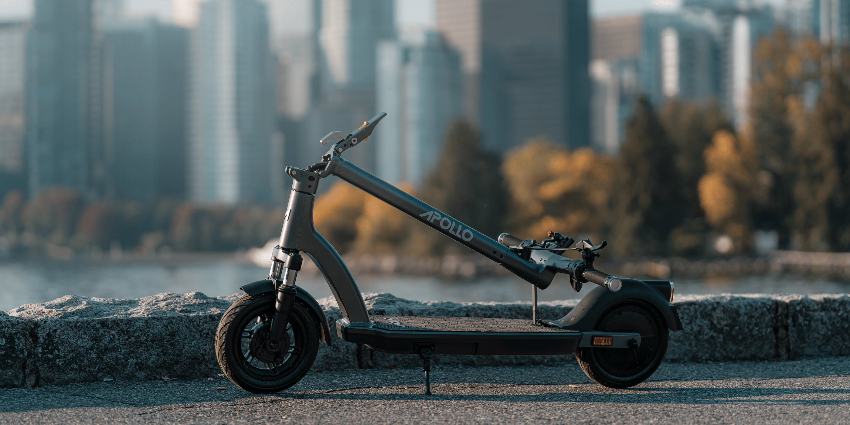An Apollo collapsible electric scooter parked next to a lake within a city area.