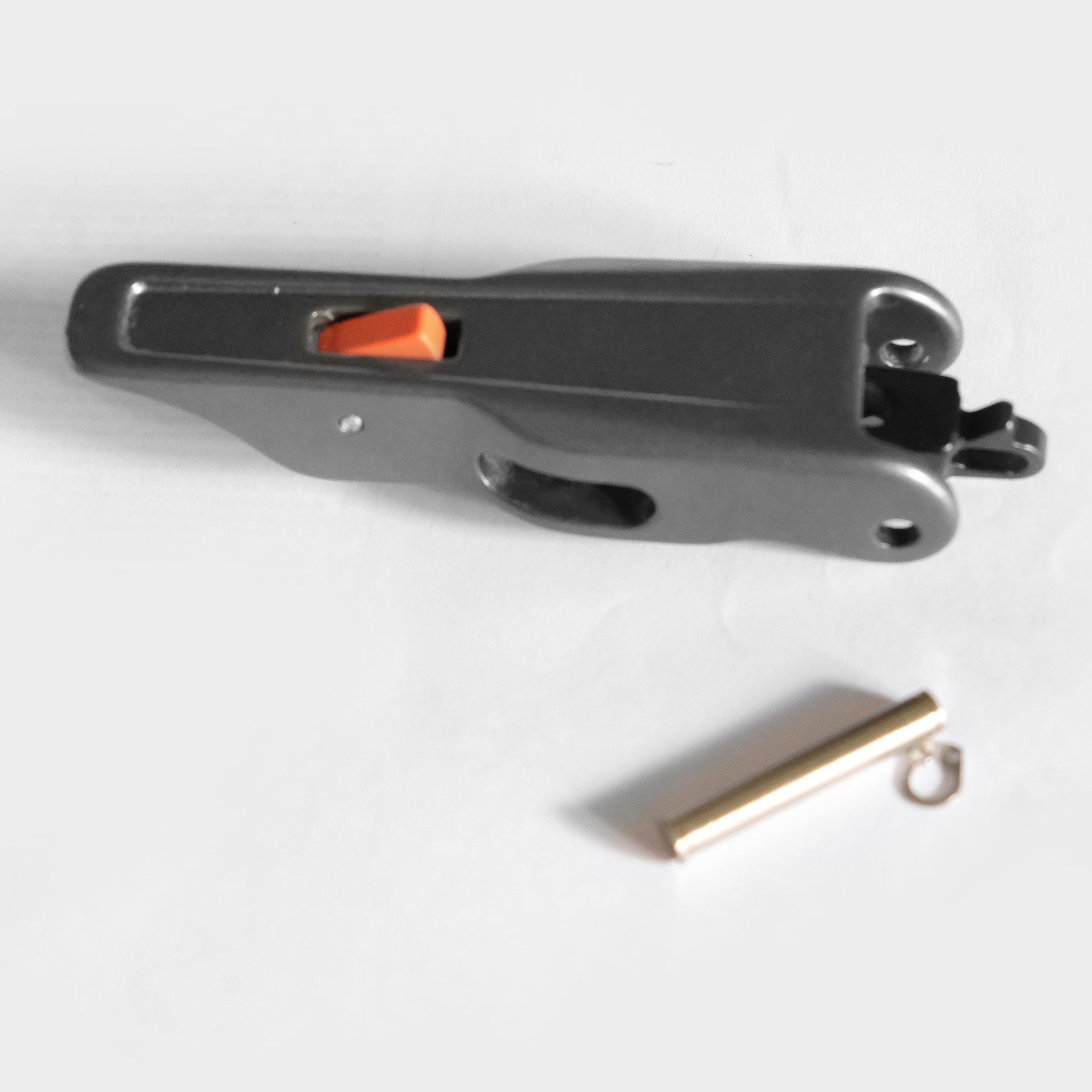 A black plastic tool with an orange button and a golden pin-like tool in the front