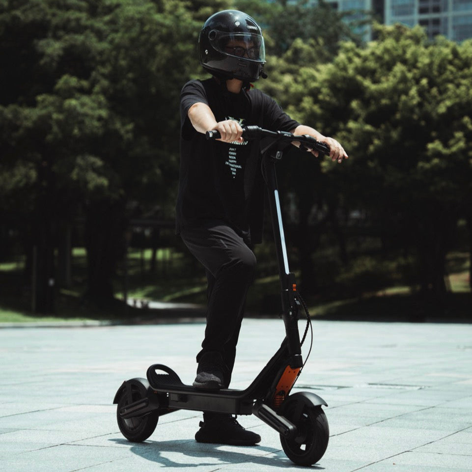 Person riding an electric scooter in an urban setting with trees and buildings in the background