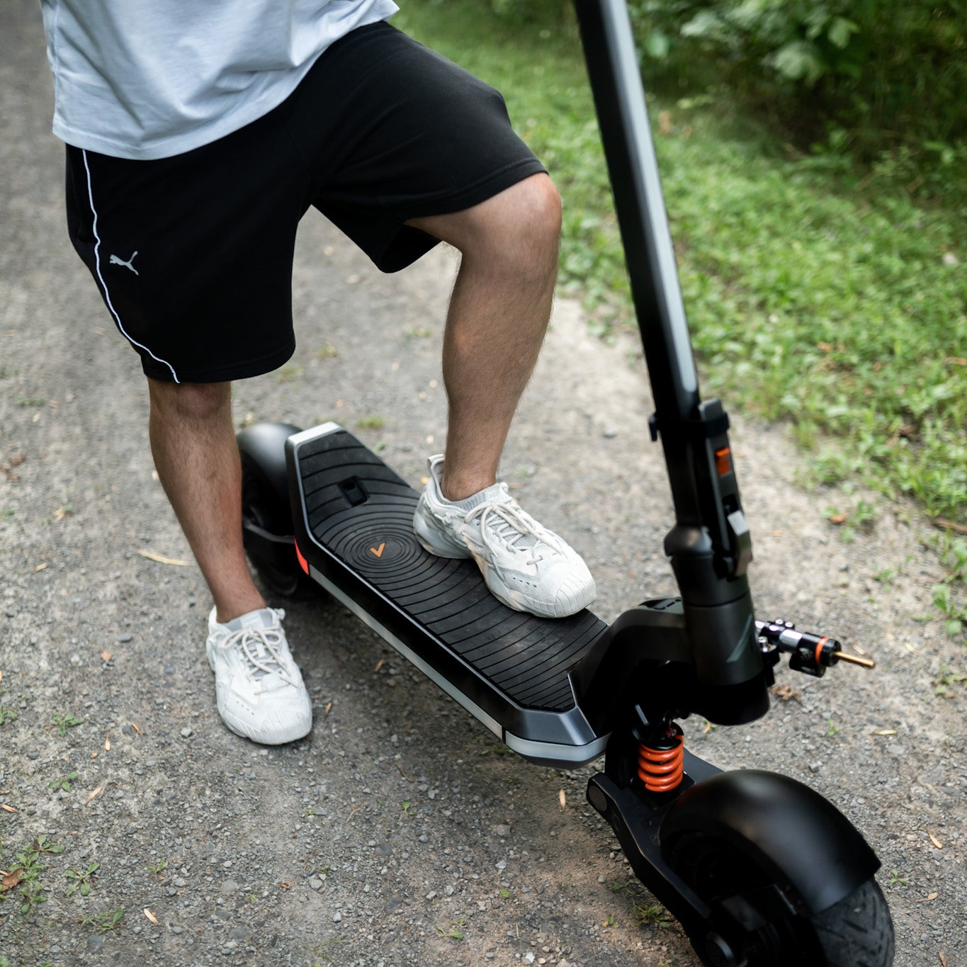 Person riding a black electric scooter on a paved path with grass on the side.