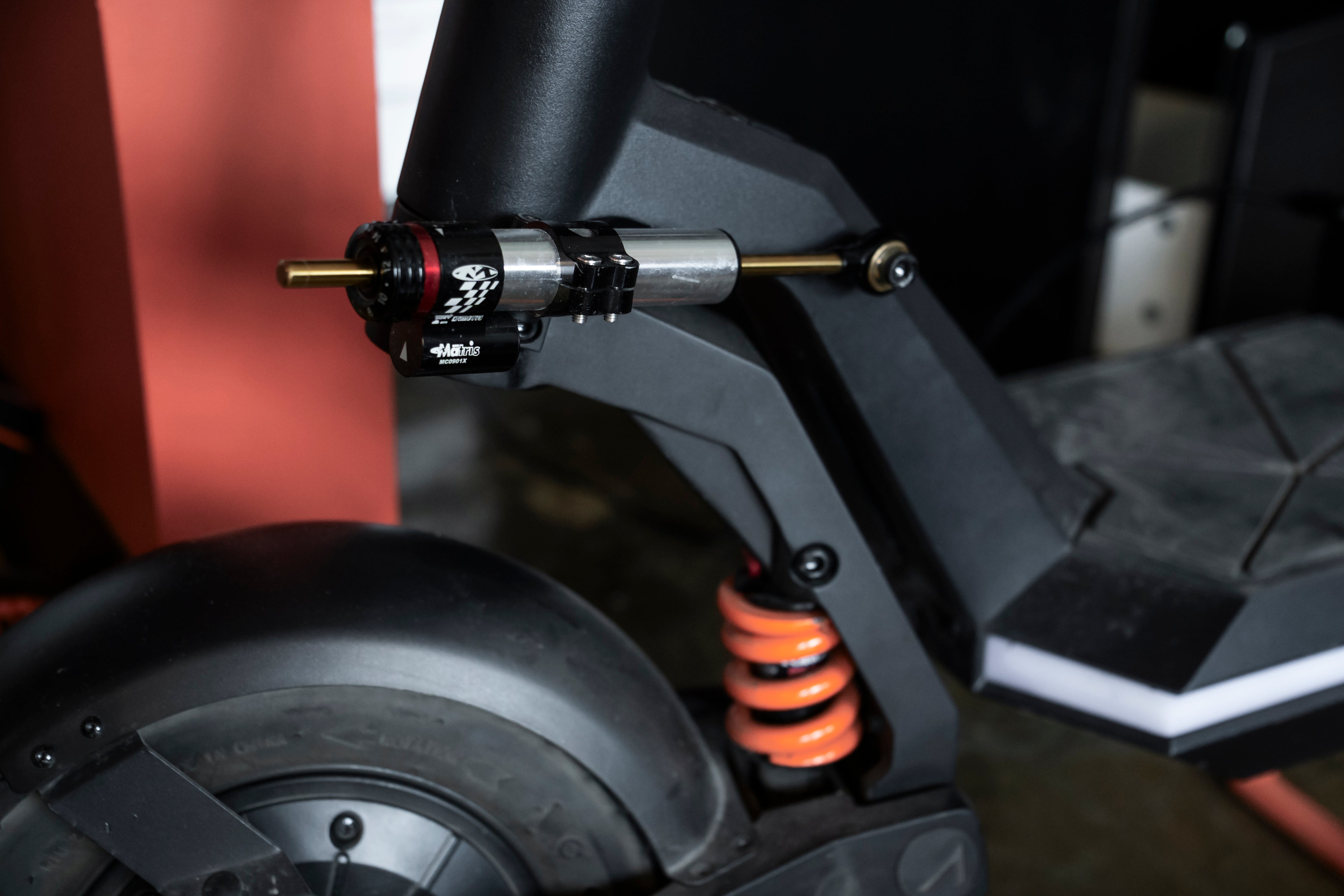 Close-up view of the front suspension on a scooter with black body, red and black handlebar grip and orange spring