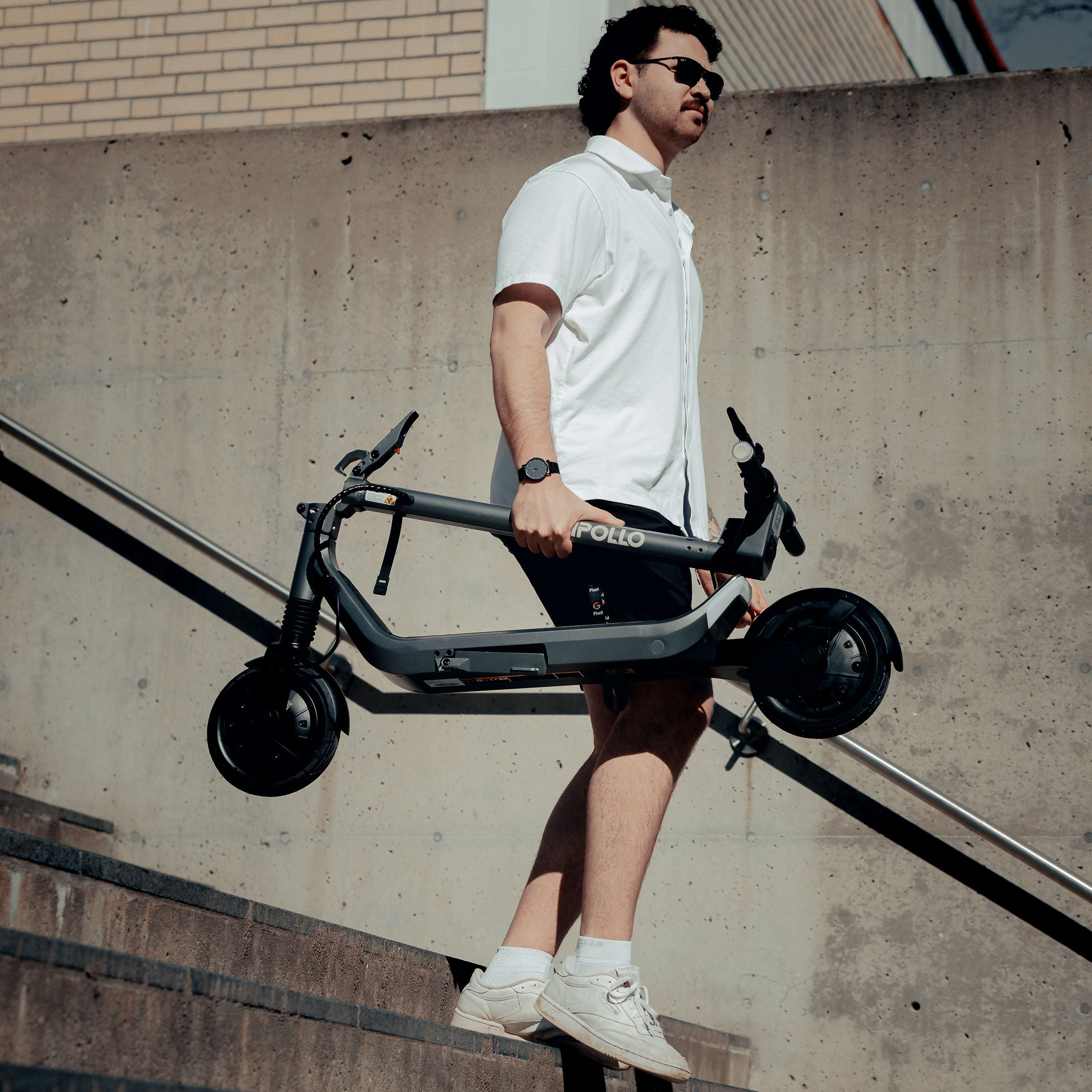 Man holding a folded electric scooter against a concrete wall.