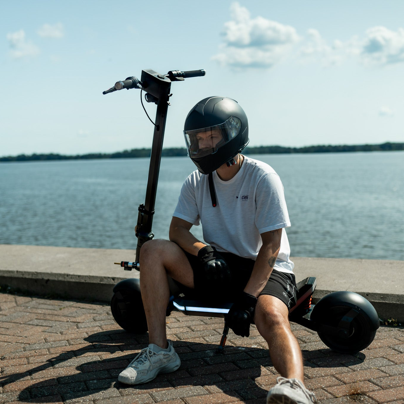 Person sitting on a scooter by a waterfront with a helmet on