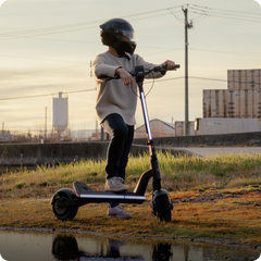Person riding an electric scooter in an open area with buildings in the background
