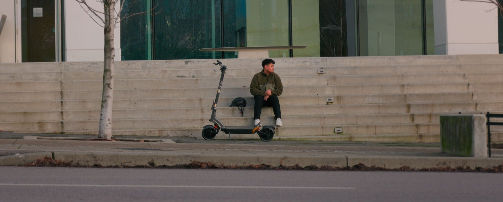 man city outside of a building in the building stairs with his Apollo City electric scooter parked in front of him